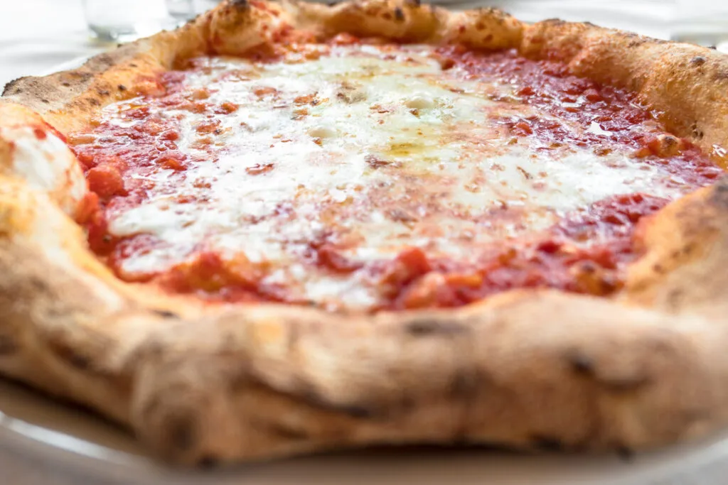 Pizza margherita integrale fatta in casa con pomodoro, mozzarella light e basilico fresco su pietra refrattaria, stile RicetteFit.