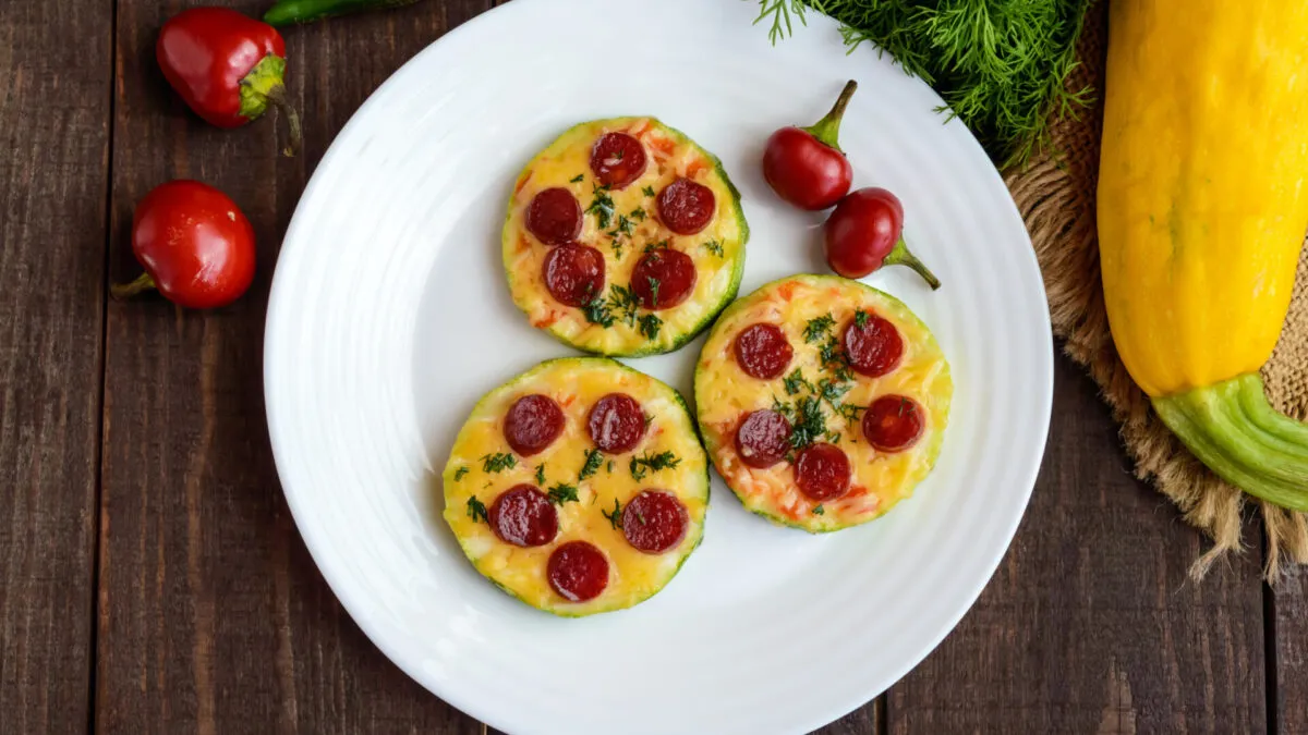 Pizzette di zucchine al forno con pomodoro, mozzarella light e origano, disposte su una teglia moderna, stile RicetteFit.