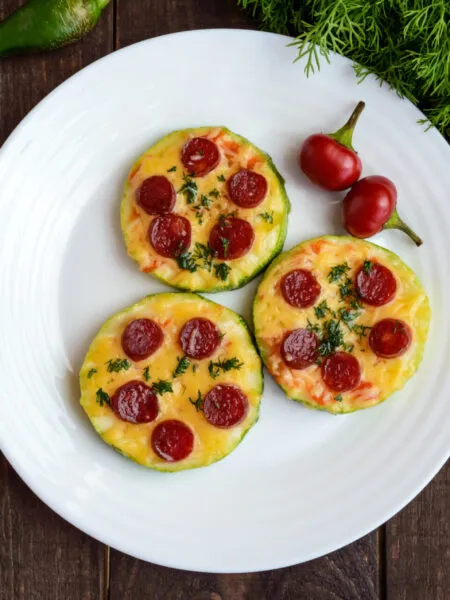 Pizzette di zucchine al forno con pomodoro, mozzarella light e origano, disposte su una teglia moderna, stile RicetteFit.