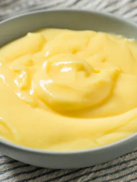 Crema pasticcera fit fatta in casa in una ciotola moderna, guarnita con frutti di bosco e scorza d'arancia, stile RicetteFit.