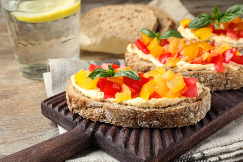 Crostini di pane integrale con hummus di ceci e fiocchi di latte freschi, decorati con granella di pistacchi e paprika, stile RicetteFit.