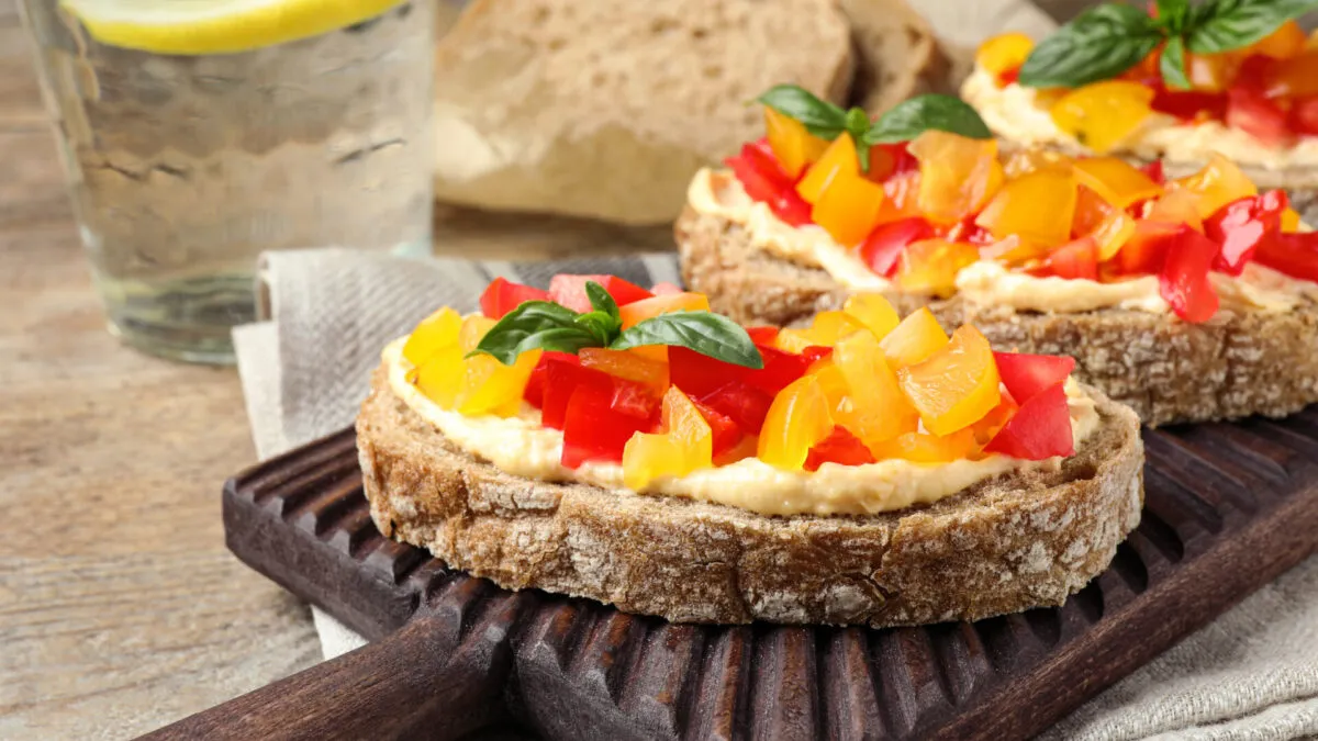 Crostini di pane integrale con hummus di ceci e fiocchi di latte freschi, decorati con granella di pistacchi e paprika, stile RicetteFit.