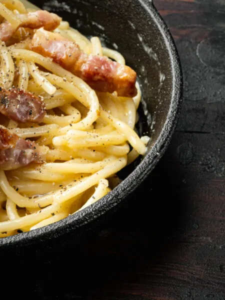 Pasta alla carbonara fit con crema di uova e pecorino leggero, guarnita con cubetti di bresaola croccante o guanciale magro, stile RicetteFit.