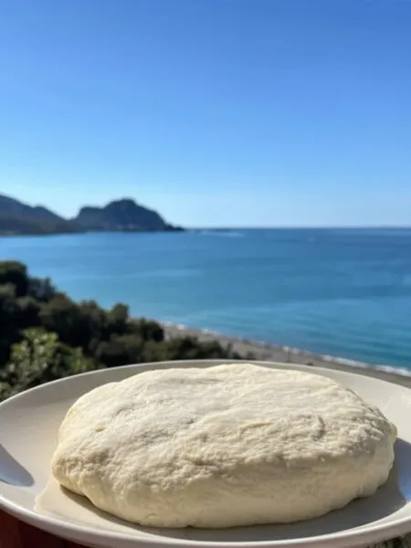 Impasto pizza senza glutine fit su piatto con mare di Cefalù sullo sfondo