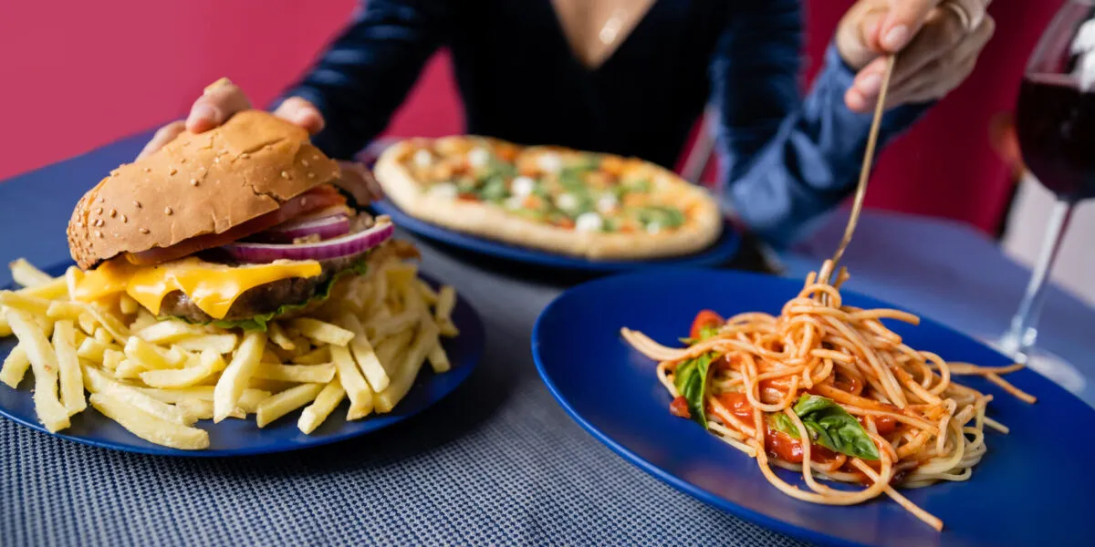 Hamburger con patatine fritte accanto a un piatto di spaghetti al pomodoro, esempio di confronto tra cibo spazzatura e alimentazione sana.