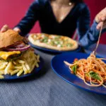 Hamburger con patatine fritte accanto a un piatto di spaghetti al pomodoro, esempio di confronto tra cibo spazzatura e alimentazione sana.