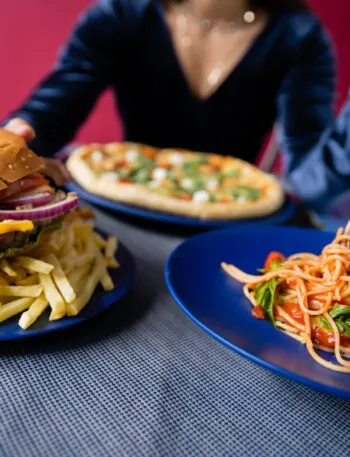 Hamburger con patatine fritte accanto a un piatto di spaghetti al pomodoro, esempio di confronto tra cibo spazzatura e alimentazione sana.