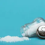 Saliera rovesciata con cristalli di sale sparsi, immagine che rappresenta come rimediare a un piatto troppo salato