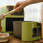 Friggitrice ad aria moderna con cestello estraibile mentre viene inserita una bistecca con una pinza da cucina.