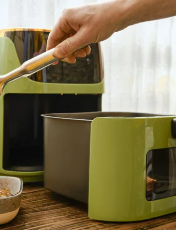 Friggitrice ad aria moderna con cestello estraibile mentre viene inserita una bistecca con una pinza da cucina.