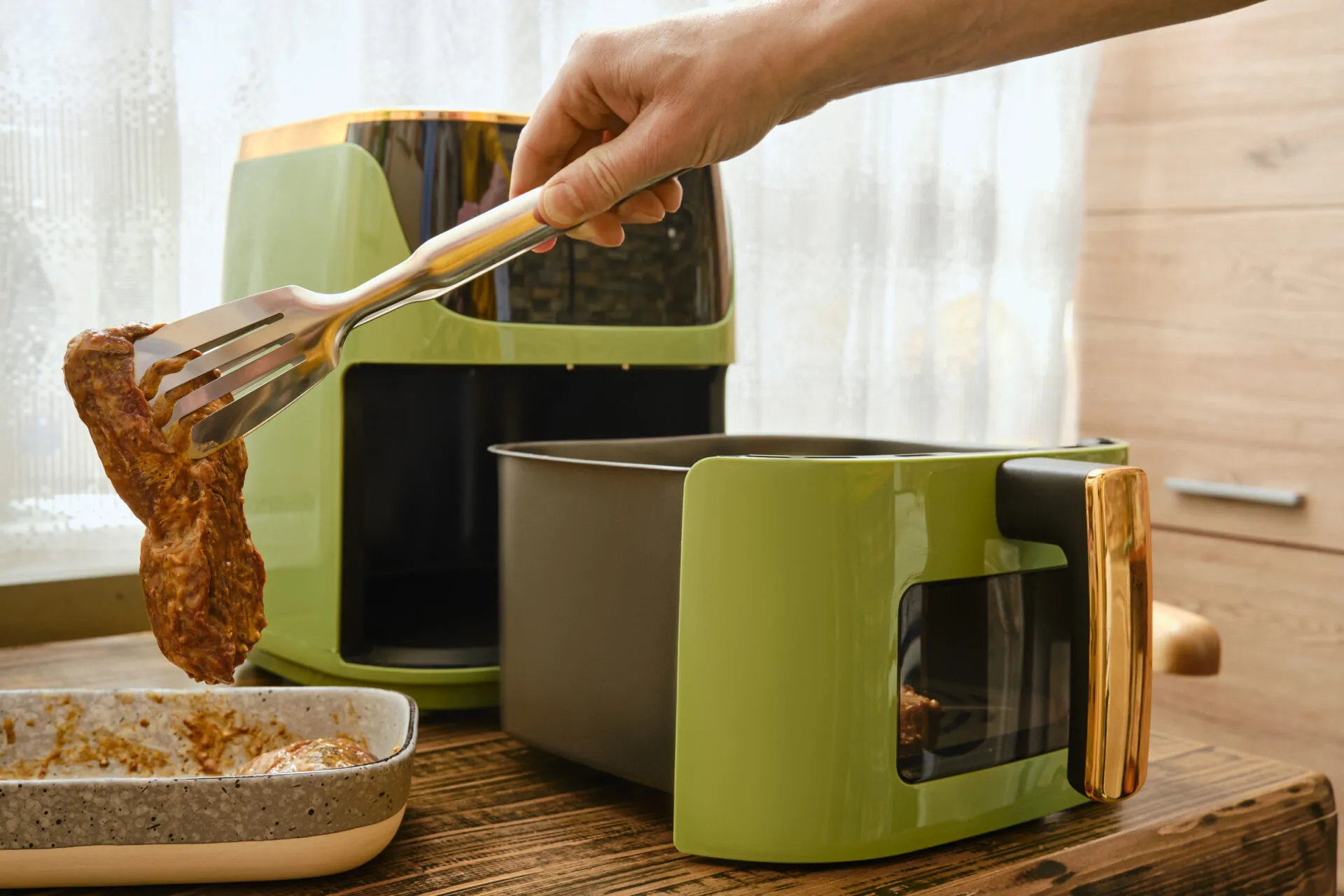 Friggitrice ad aria moderna con cestello estraibile mentre viene inserita una bistecca con una pinza da cucina.