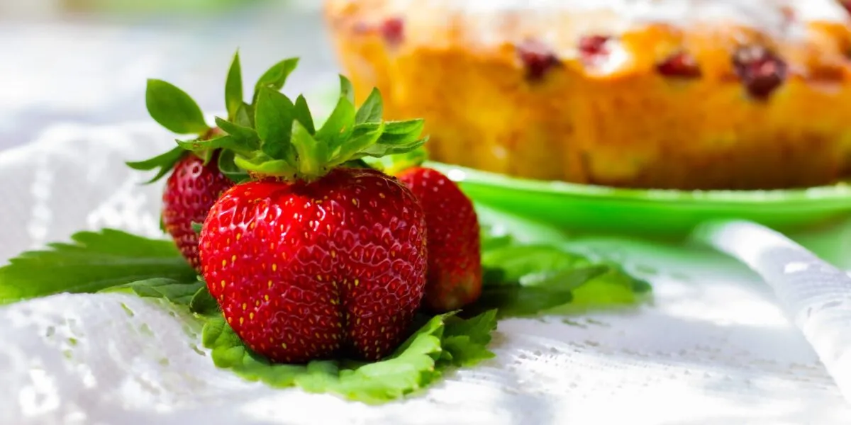 Primo piano di fragole fresche con torta sullo sfondo sfocato, immagine perfetta per dolci semplici e golosi con le fragole
