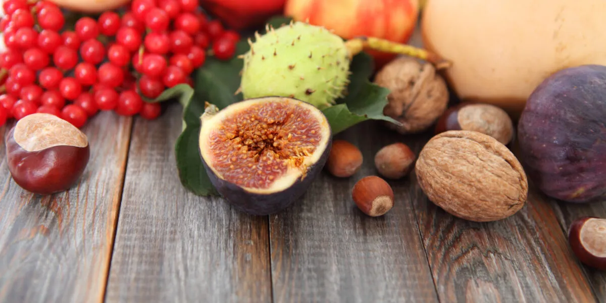 Frutta di stagione autunnale con fichi, castagne, mele, noci e bacche rosse disposta su un tavolo in legno
