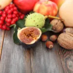Frutta di stagione autunnale con fichi, castagne, mele, noci e bacche rosse disposta su un tavolo in legno