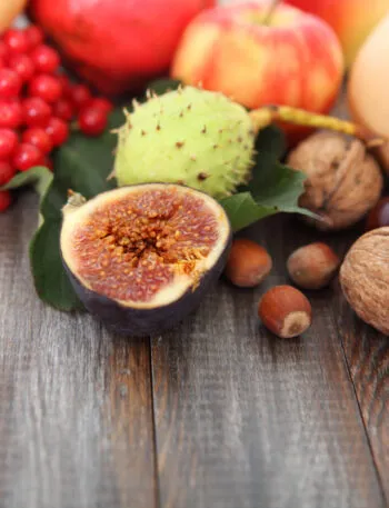 Frutta di stagione autunnale con fichi, castagne, mele, noci e bacche rosse disposta su un tavolo in legno