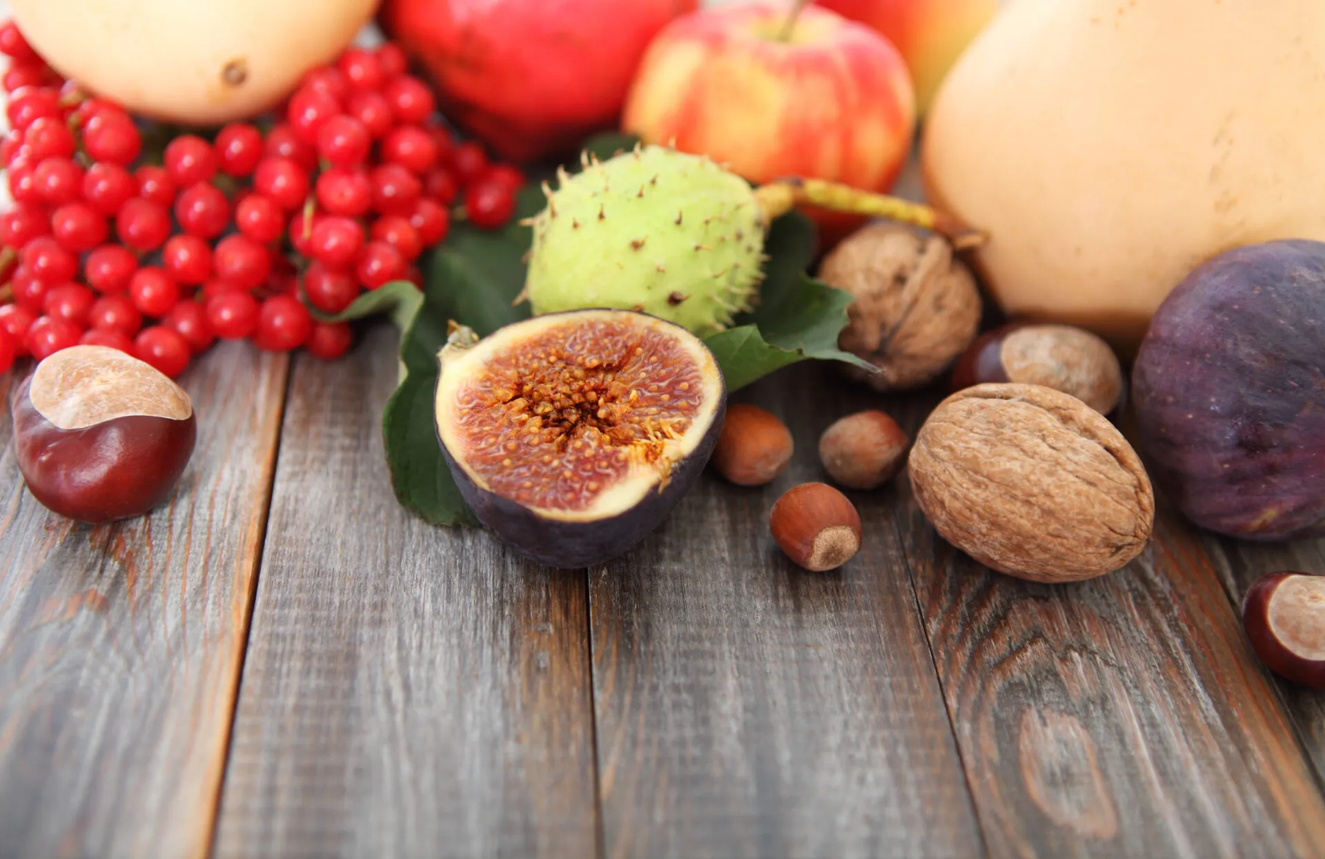 Frutta di stagione autunnale con fichi, castagne, mele, noci e bacche rosse disposta su un tavolo in legno