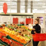 Donna che fa la spesa nel reparto ortofrutta di Lidl tra pomodori, peperoni e verdure fresche in offerta nel volantino di maggio.