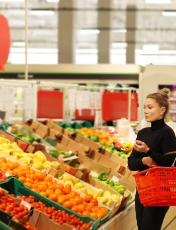 Donna che fa la spesa nel reparto ortofrutta di Lidl tra pomodori, peperoni e verdure fresche in offerta nel volantino di maggio.