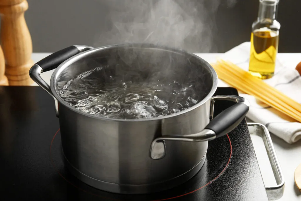 Pentola con acqua bollente sul fornello, metodo di cottura tradizionale utilizzato per pasta, riso e verdure.