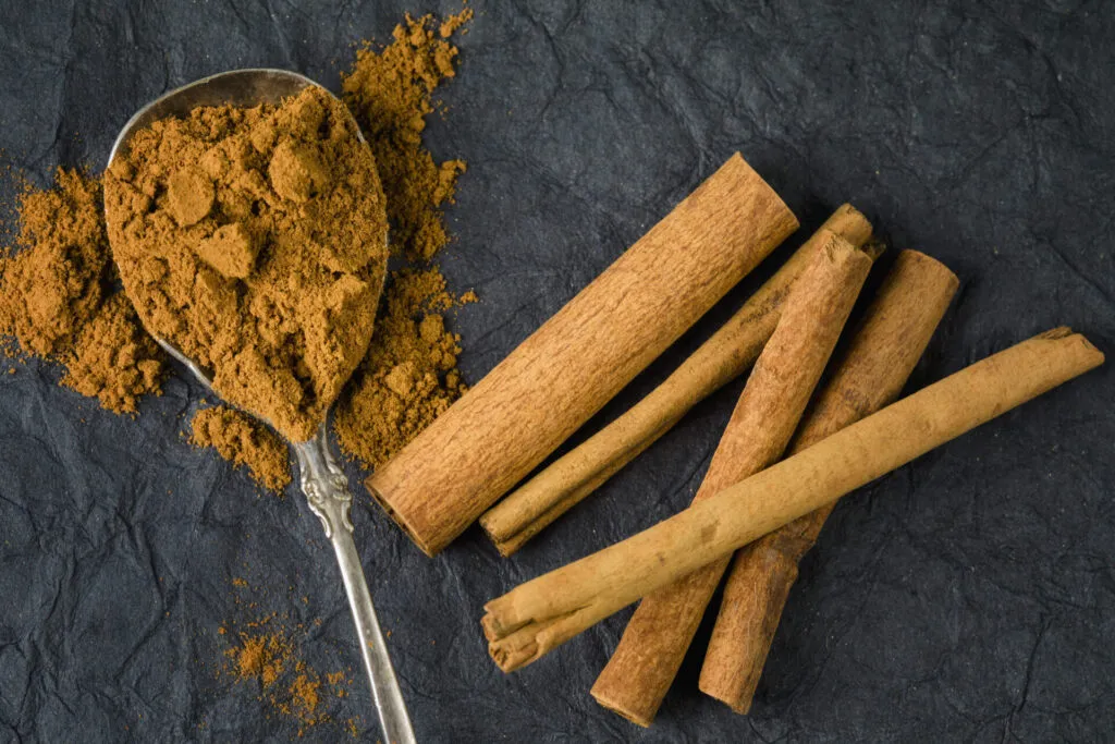 Cucchiaiata di cannella in polvere e stecche di cannella su una superficie scura, utilizzate come rimedio naturale per allontanare le formiche dalla cucina.