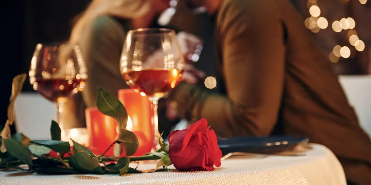 Coppia durante una cena romantica a lume di candela con calici di vino, candele accese e una rosa rossa sulla tavola.