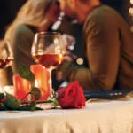 Coppia durante una cena romantica a lume di candela con calici di vino, candele accese e una rosa rossa sulla tavola.