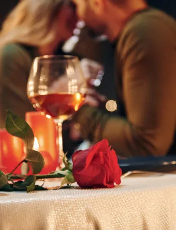 Coppia durante una cena romantica a lume di candela con calici di vino, candele accese e una rosa rossa sulla tavola.