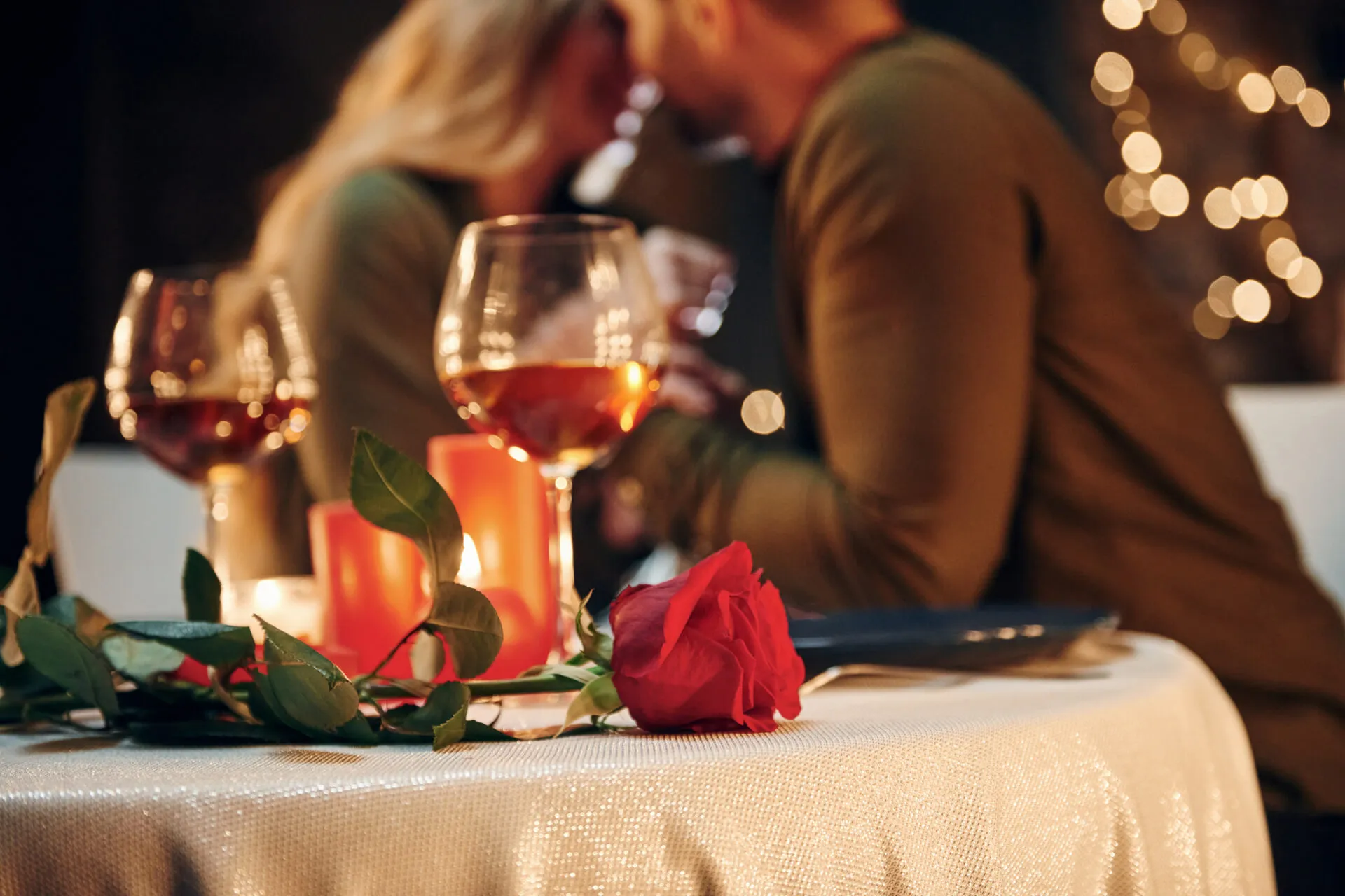 Coppia durante una cena romantica a lume di candela con calici di vino, candele accese e una rosa rossa sulla tavola.