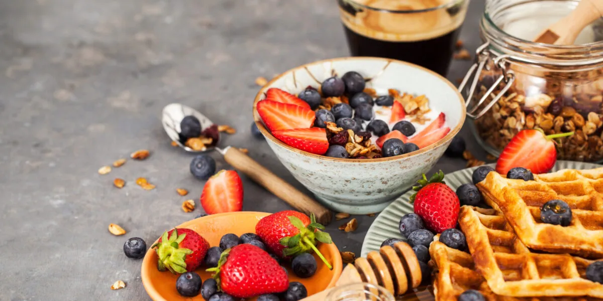 Colazione fit con yogurt, granola, fragole, mirtilli, waffle integrali e caffè per iniziare la giornata con energia e leggerezza.