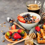 Colazione fit con yogurt, granola, fragole, mirtilli, waffle integrali e caffè per iniziare la giornata con energia e leggerezza.
