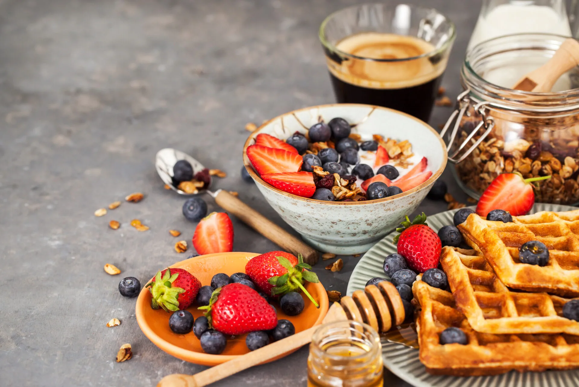 Colazione fit con yogurt, granola, fragole, mirtilli, waffle integrali e caffè per iniziare la giornata con energia e leggerezza.