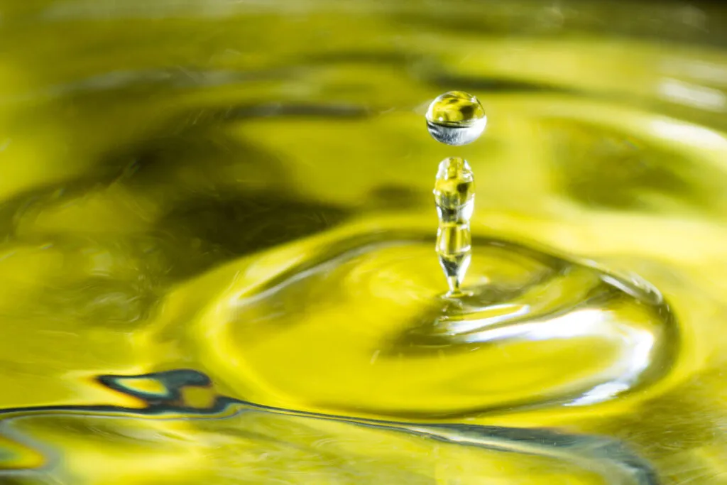 Goccia di olio extravergine d'oliva con riflessi dorati su una superficie liquida, simbolo della qualità dell'olio EVO.