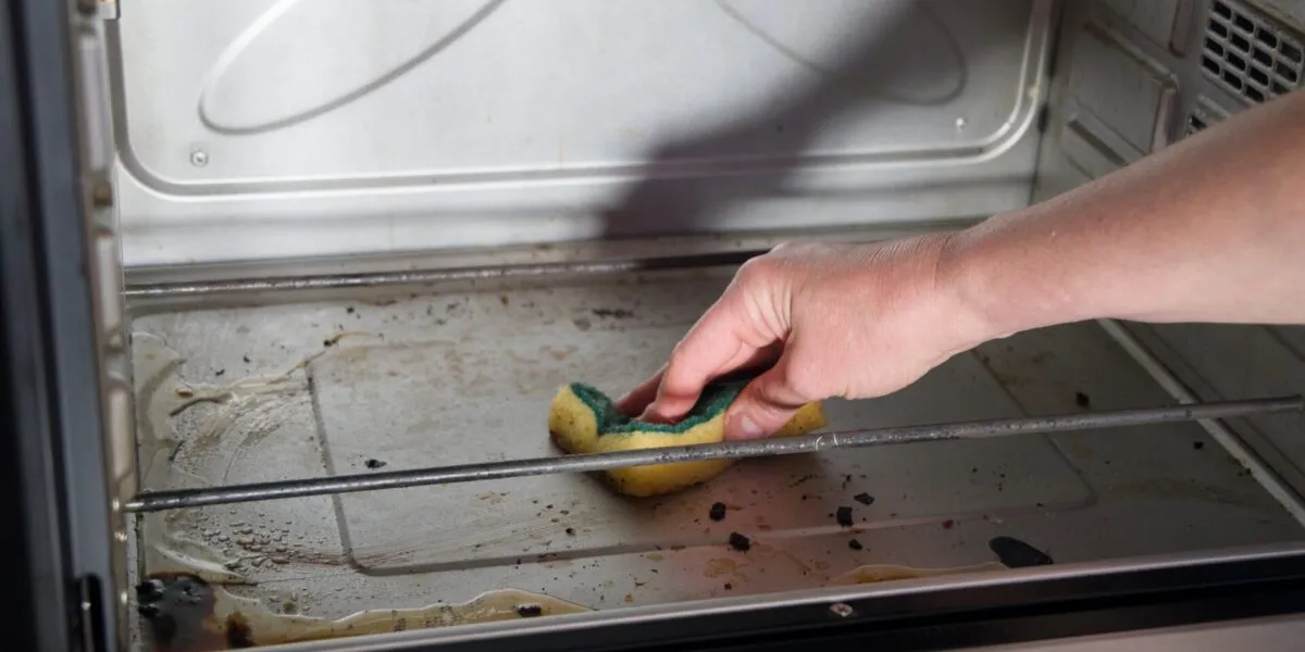 Pulizia del forno con una spugna su una superficie interna leggermente incrostata, per rimuovere grasso e residui di cottura in modo semplice ed efficace.