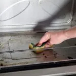Pulizia del forno con una spugna su una superficie interna leggermente incrostata, per rimuovere grasso e residui di cottura in modo semplice ed efficace.