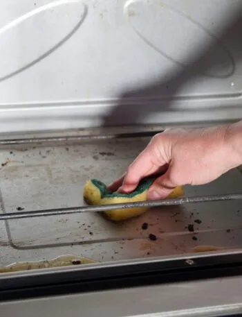 Pulizia del forno con una spugna su una superficie interna leggermente incrostata, per rimuovere grasso e residui di cottura in modo semplice ed efficace.
