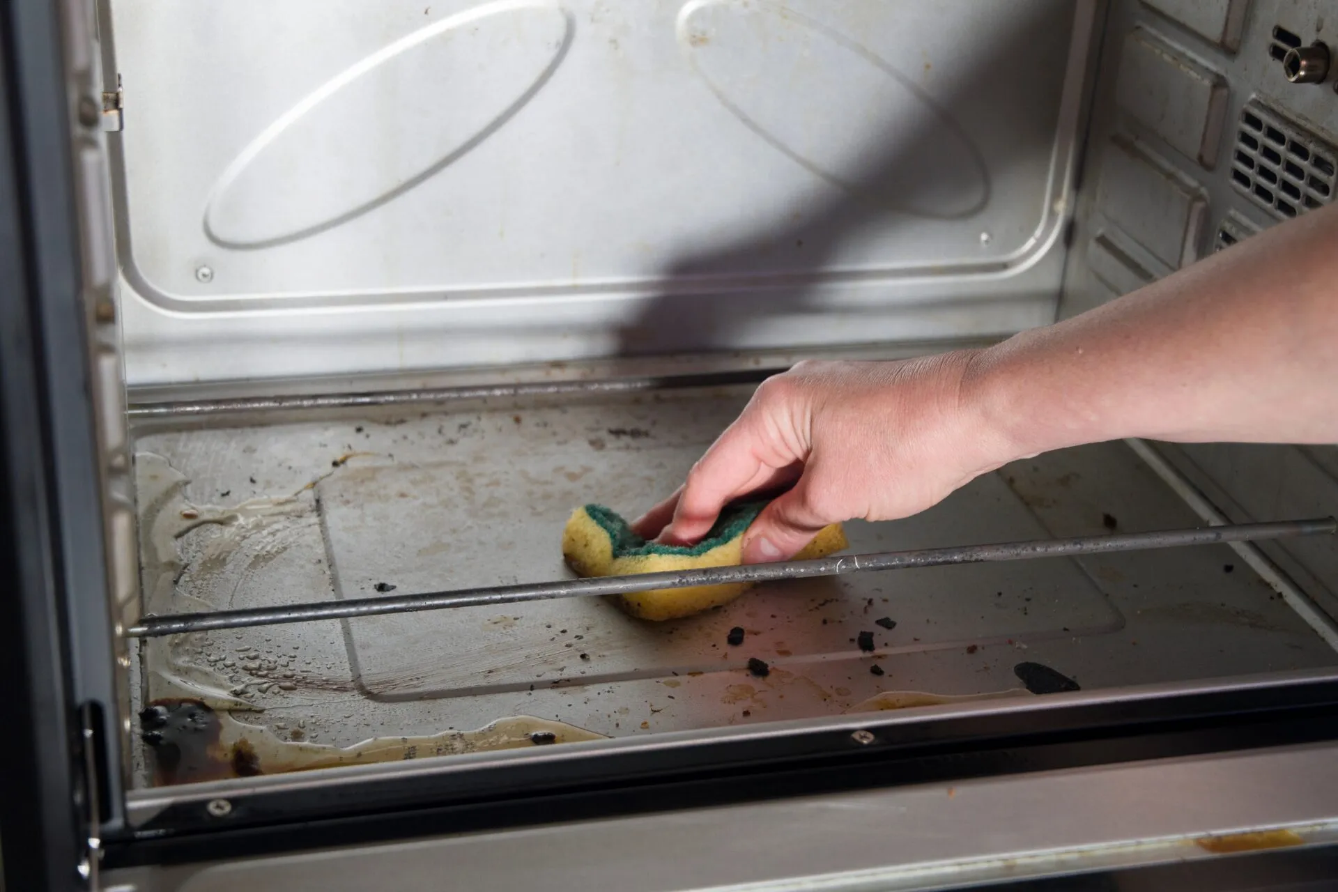 Pulizia del forno con una spugna su una superficie interna leggermente incrostata, per rimuovere grasso e residui di cottura in modo semplice ed efficace.