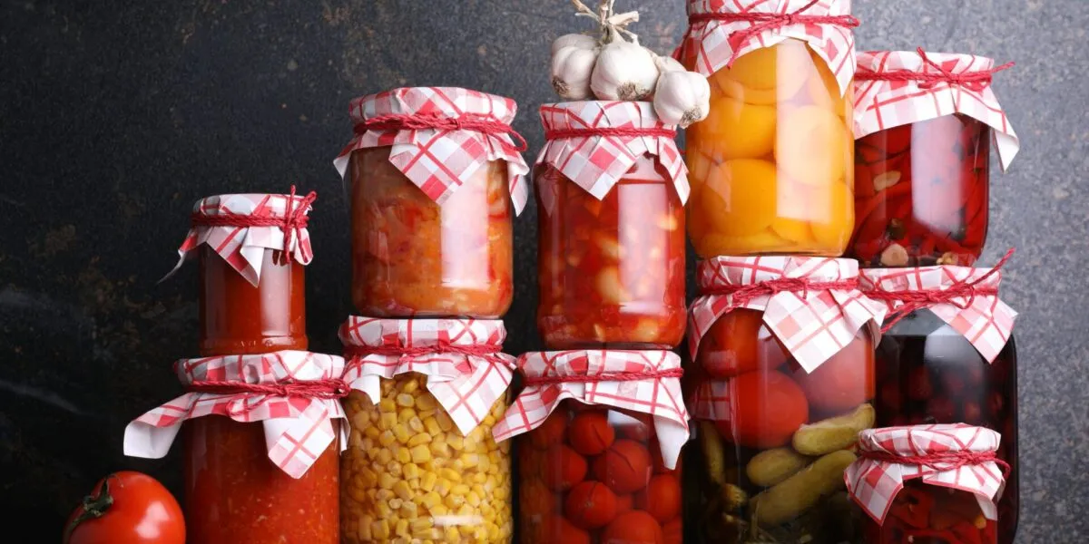 Barattoli di conserve fatte in casa con pomodori, peperoni, cetrioli e verdure sott'aceto disposti su un tavolo, esempio di preparazione sicura delle conserve domestiche.