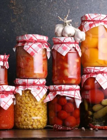 Barattoli di conserve fatte in casa con pomodori, peperoni, cetrioli e verdure sott'aceto disposti su un tavolo, esempio di preparazione sicura delle conserve domestiche.