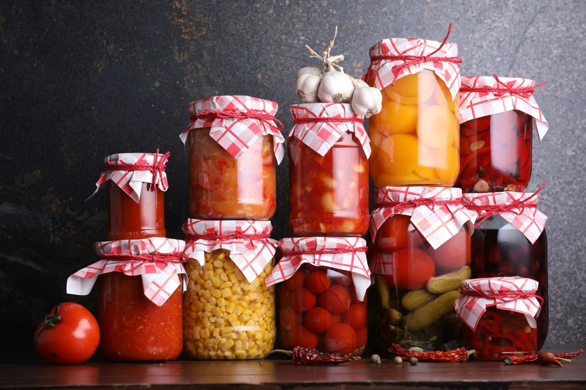 Barattoli di conserve fatte in casa con pomodori, peperoni, cetrioli e verdure sott'aceto disposti su un tavolo, esempio di preparazione sicura delle conserve domestiche.