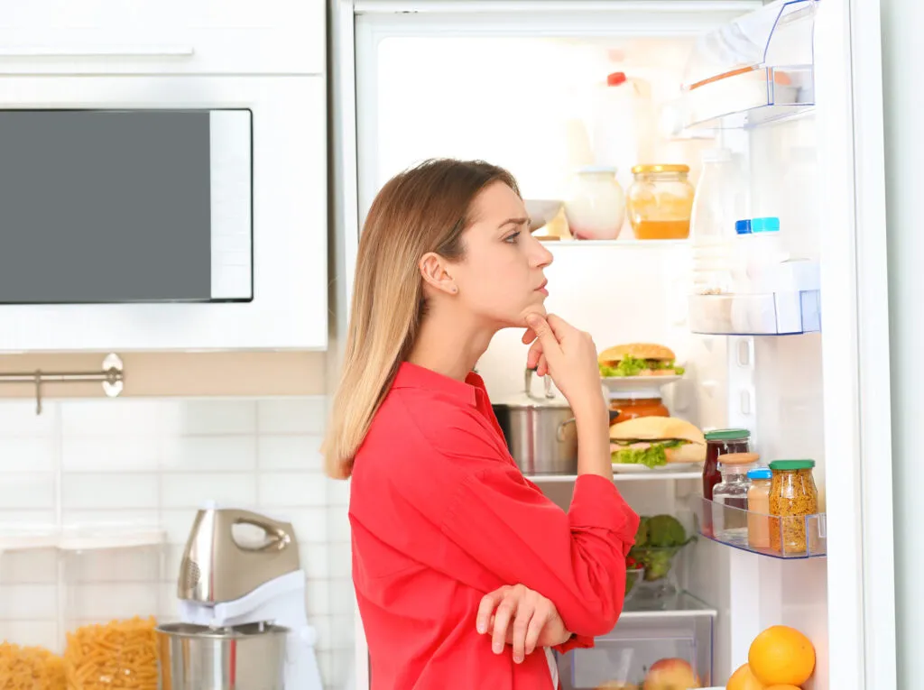 Donna davanti a un frigorifero aperto mentre controlla avanzi e ingredienti da utilizzare per preparare ricette anti-spreco.