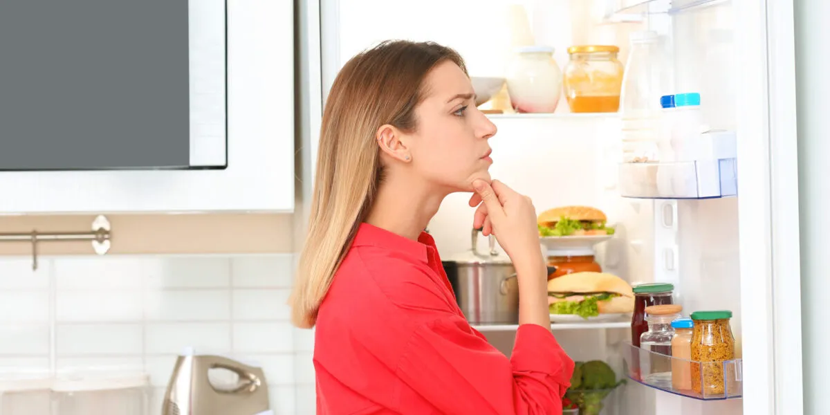 Donna davanti a un frigorifero aperto mentre controlla avanzi e ingredienti da utilizzare per preparare ricette anti-spreco.