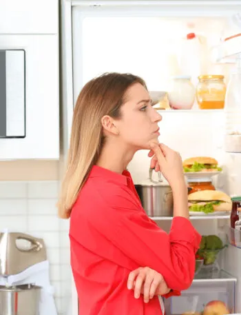 Donna davanti a un frigorifero aperto mentre controlla avanzi e ingredienti da utilizzare per preparare ricette anti-spreco.