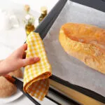 Pagnotta di pane appena sfornata su una teglia con carta forno, pronta per essere rigenerata in forno dopo lo scongelamento.