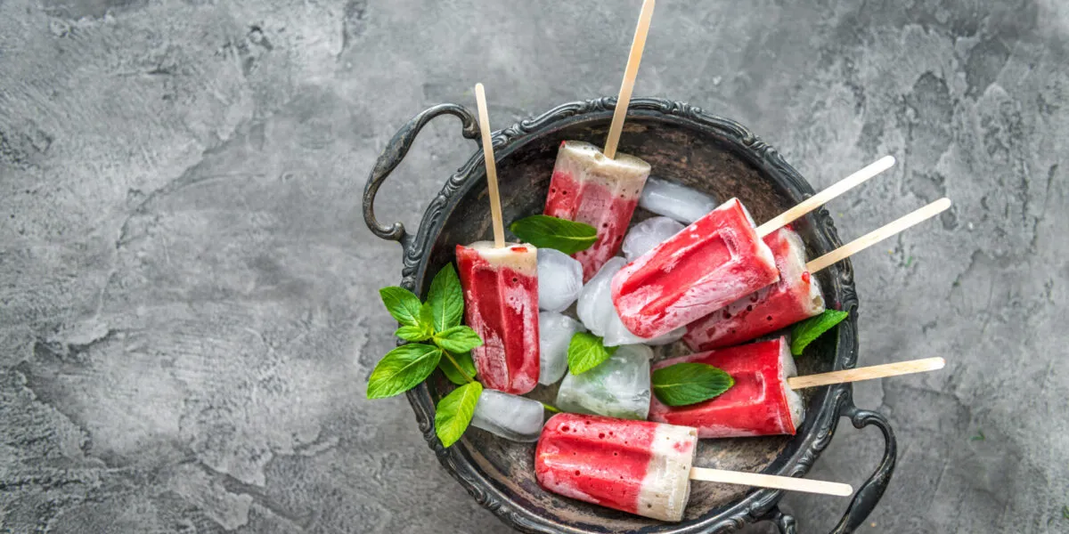Ghiaccioli fatti in casa alla frutta e yogurt serviti con ghiaccio e foglie di menta, preparati con ingredienti naturali senza stampi professionali.