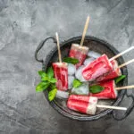 Ghiaccioli fatti in casa alla frutta e yogurt serviti con ghiaccio e foglie di menta, preparati con ingredienti naturali senza stampi professionali.