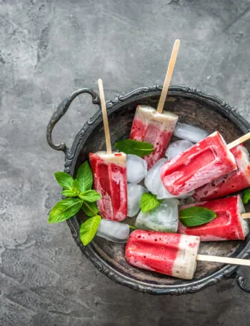 Ghiaccioli fatti in casa alla frutta e yogurt serviti con ghiaccio e foglie di menta, preparati con ingredienti naturali senza stampi professionali.