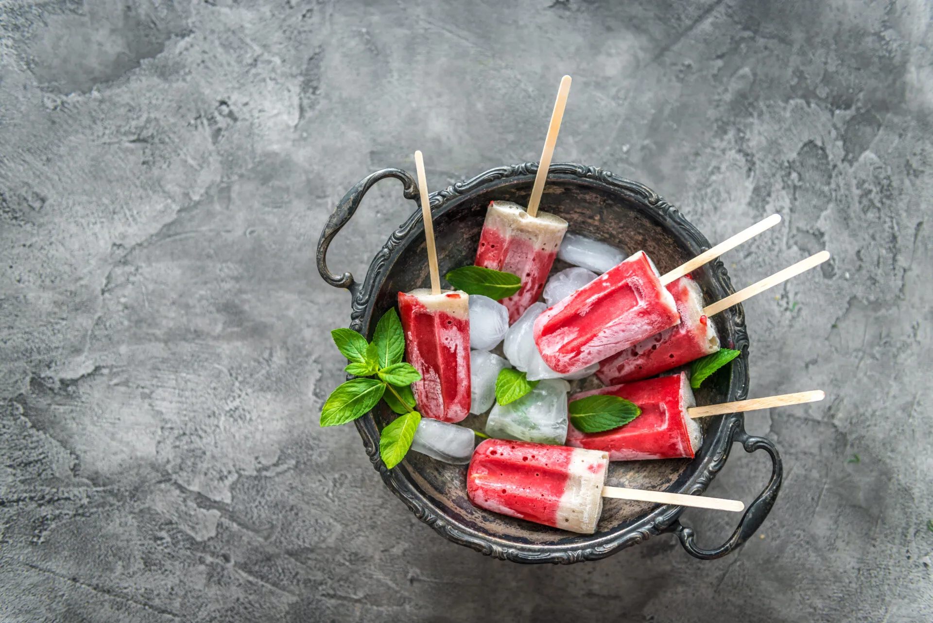 Ghiaccioli fatti in casa alla frutta e yogurt serviti con ghiaccio e foglie di menta, preparati con ingredienti naturali senza stampi professionali.