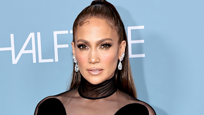 Jennifer Lopez posa sul red carpet con capelli raccolti, orecchini pendenti e un elegante abito nero dal design moderno.