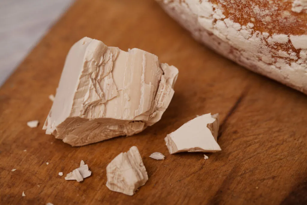 Lievito di birra fresco in cubetto con pane artigianale sullo sfondo, agente lievitante naturale ideale per pane, pizza, focacce e brioche.