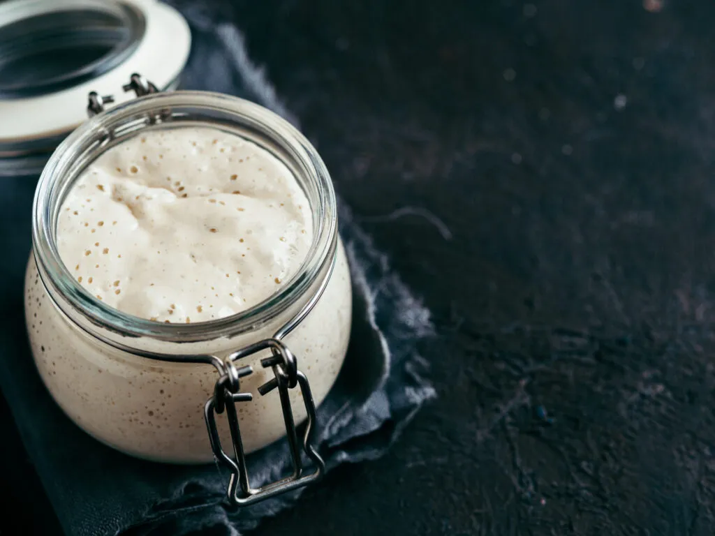 Lievito madre naturale in fermentazione all'interno di un barattolo di vetro, con bolle visibili e alveolatura attiva per pane, pizza e lievitati artigianali.